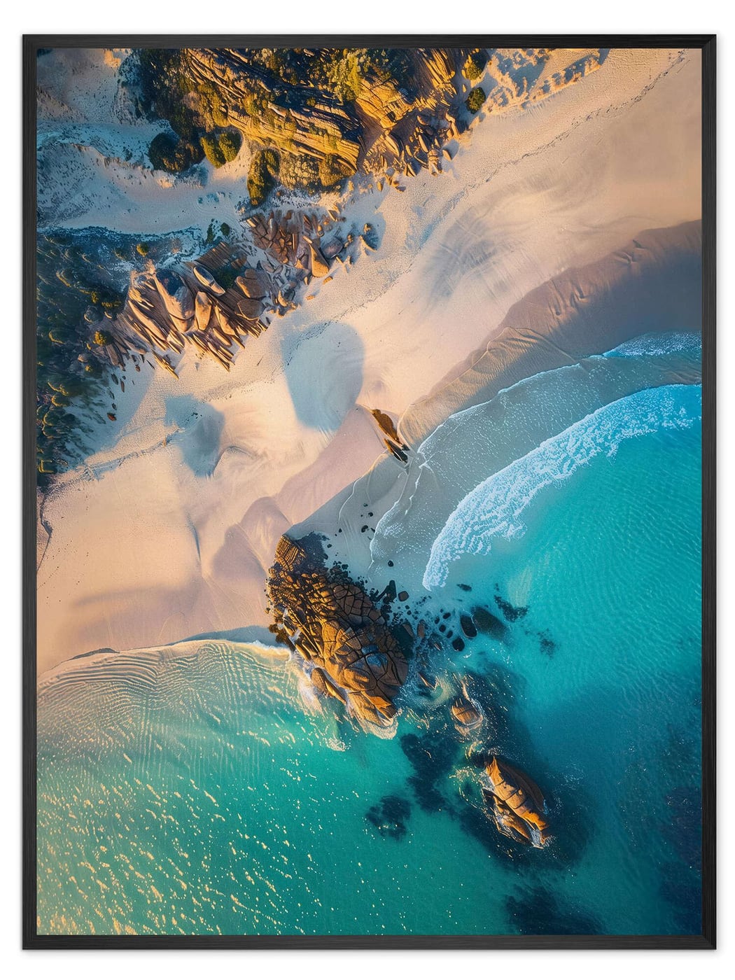 An aerial photographic print of turquoise ocean meeting pale sand and rocks, in a slim black frame